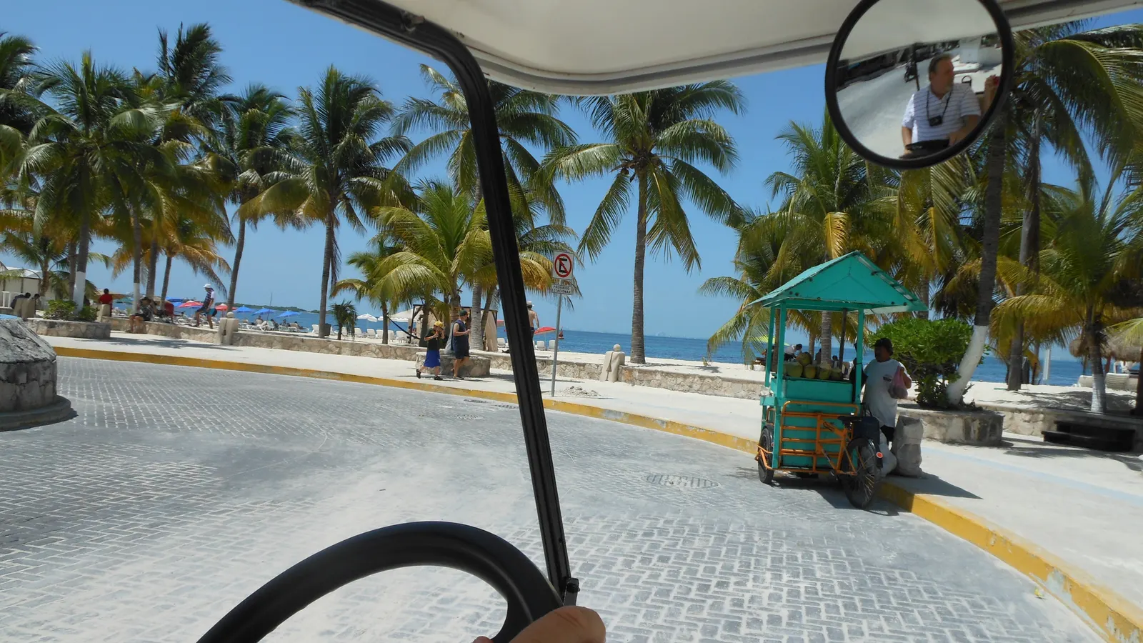 Driver's view from a golf cart on a palm-lined seaside street